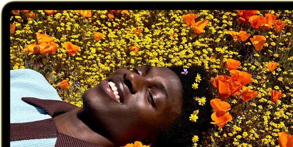 MacBook Neo, color amarillo cítrico, la pantalla muestra a una persona sonriente acostada en un campo de flores bajo el sol